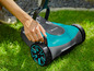 Une personne utilise une tondeuse robot Gardena bleue dans l'herbe.