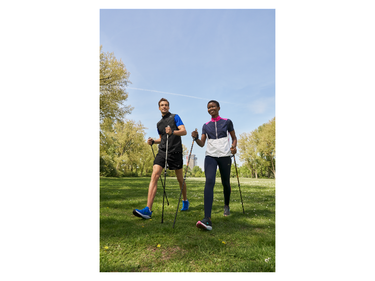 Deux personnes marchent dans un parc avec des bâtons de marche nordique.