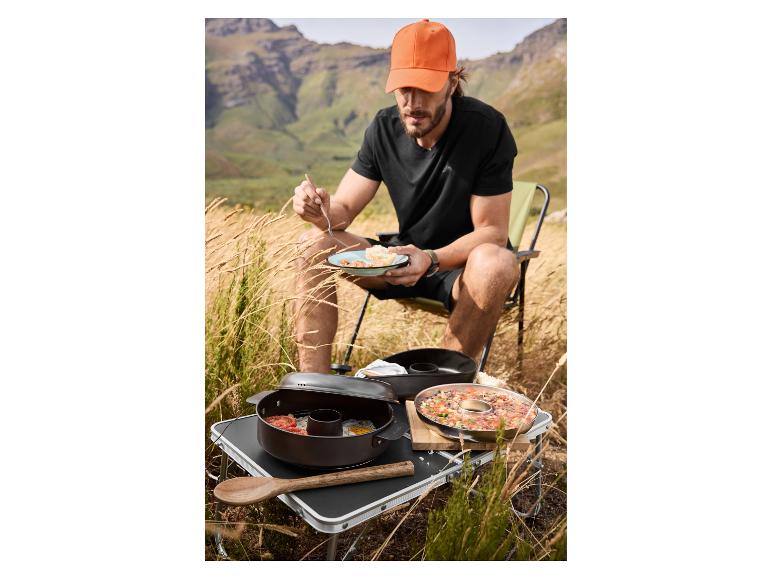 Homme mangeant en camping avec ustensiles de cuisine et nourriture sur la table.