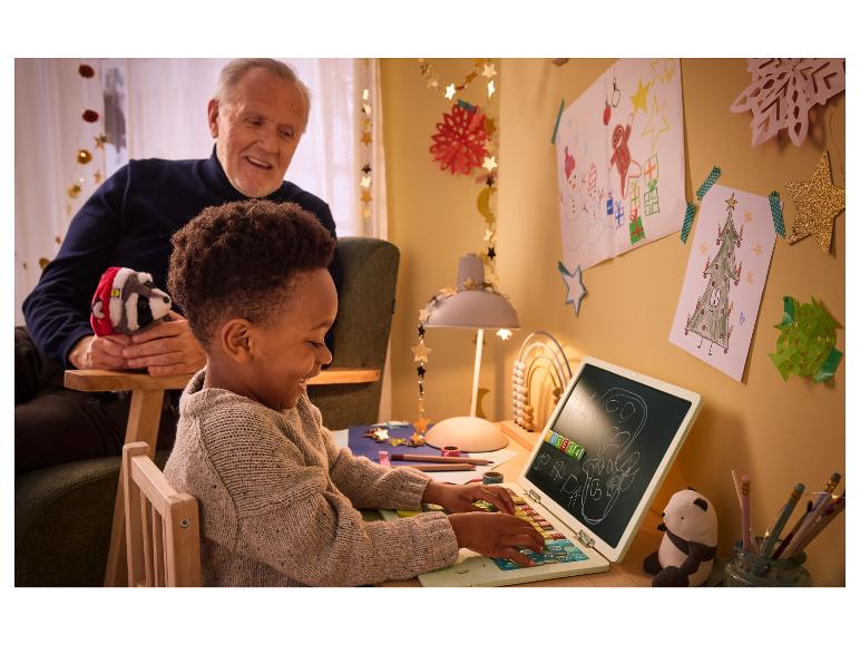 Un enfant joue avec un ordinateur portable jouet tandis que son grand-père le regarde en souriant.