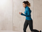 Femme en haut de sport bleu et leggings noirs en train de courir.