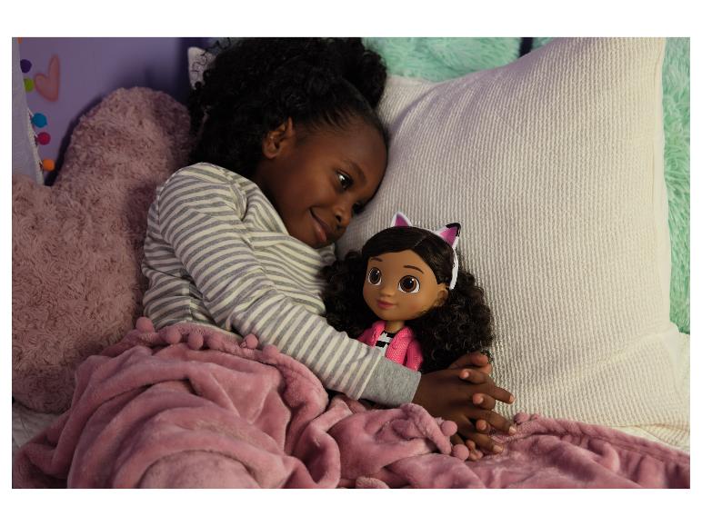 Une jeune fille en pyjama rayé câline une poupée aux oreilles de chat sous une couverture rose.