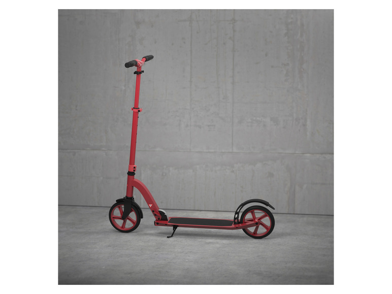 Une trottinette rouge avec des roues noires contre un mur en béton.