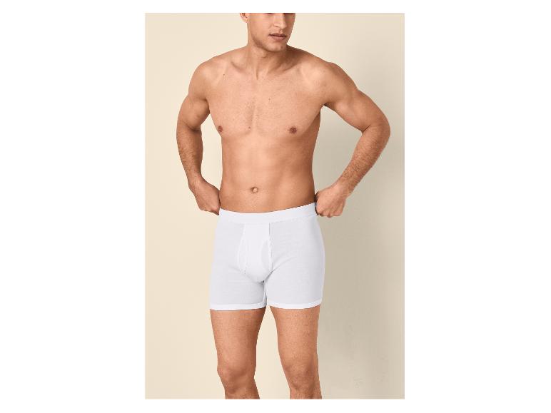 Homme torse nu en caleçon blanc, ajustant la ceinture.