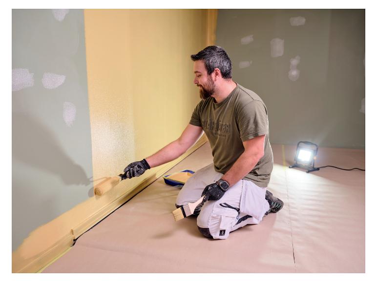 Homme peignant un mur, éclairé par la lampe de travail LIVARNO® «The Painter+».