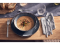 Un bol de soupe crémeuse servi avec des couverts et du pain sur une table dressée.