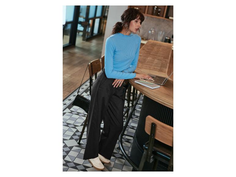 Une femme portant un pull bleu et un pantalon noir travaille sur un ordinateur portable dans un café.