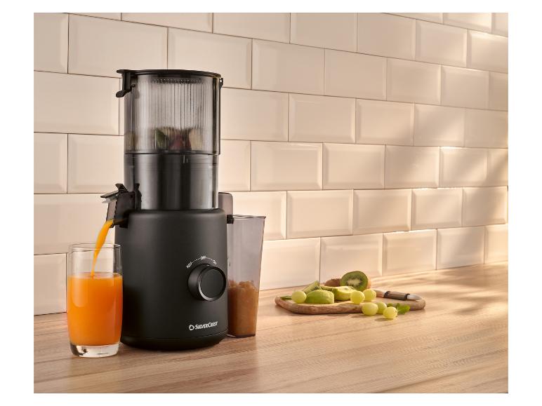 Extracteur de jus noir préparant du jus d'orange, avec des fruits frais sur la table.