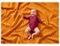 Bébé heureux en body bordeaux allongé sur une couverture orange en tricot gaufré.