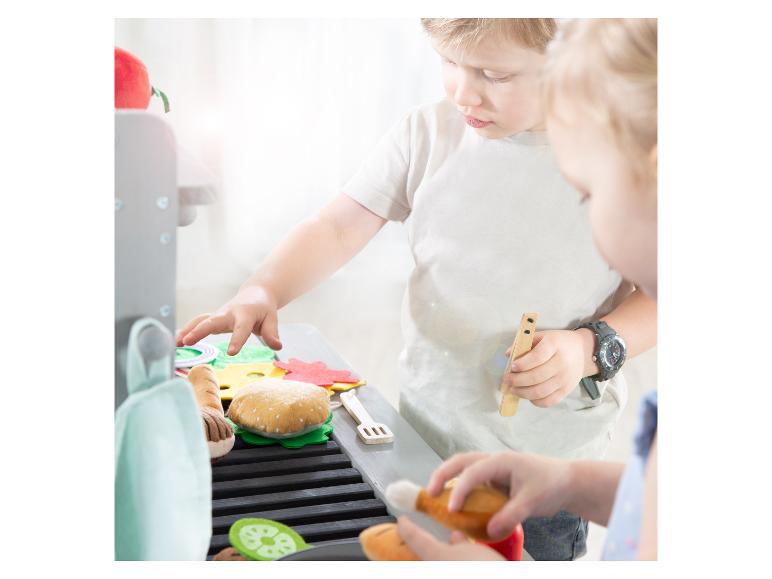 Enfants jouant avec un barbecue jouet et de la nourriture en feutre, dont un hamburger et des légumes.