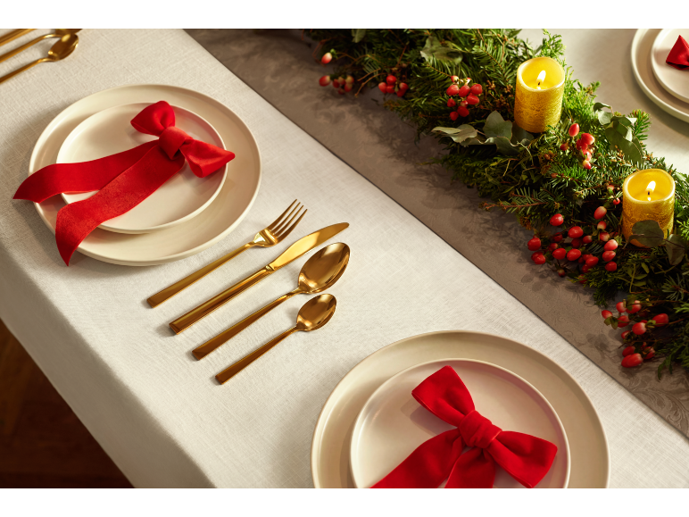 Table de Noël festive avec assiettes blanches, nœuds rouges, couverts dorés et guirlande verte