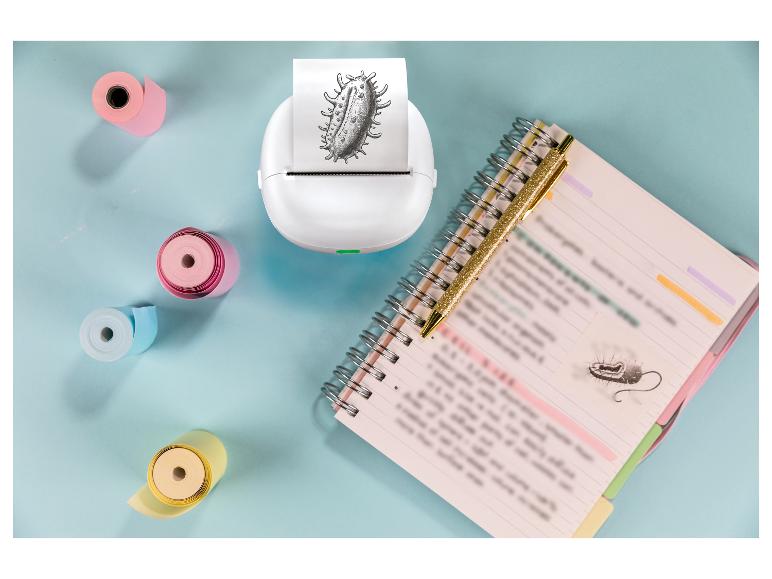 Mini-imprimante blanche avec impression de bactérie, carnet et stylo sur fond bleu.