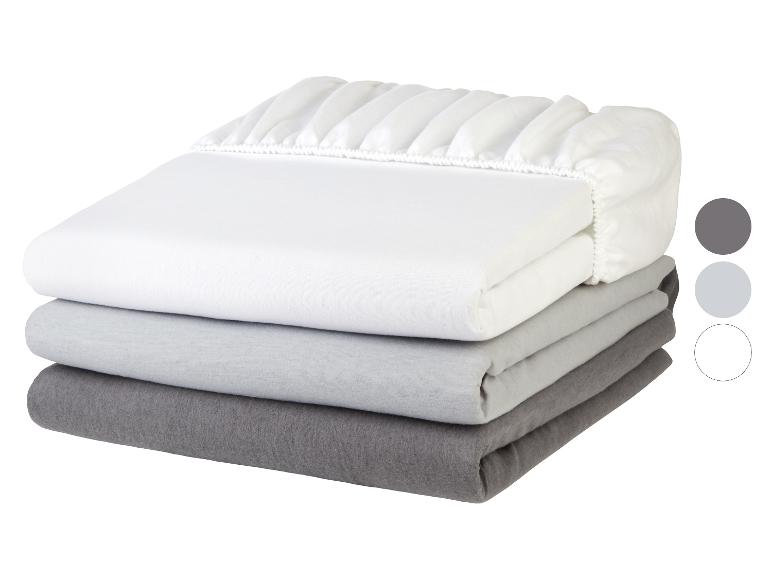 Pile de trois draps housses pliés en blanc, gris clair et gris foncé.