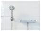 Une douche et un mitigeur thermostatique chromés sont fixés à un mur carrelé blanc.