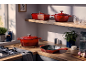 Ustensiles de cuisine en fonte rouge sur un plan de travail et une étagère en bois dans une cuisine lumineuse.