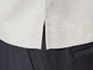 Gros plan sur une chemise beige avec des fentes, portée avec un pantalon noir.