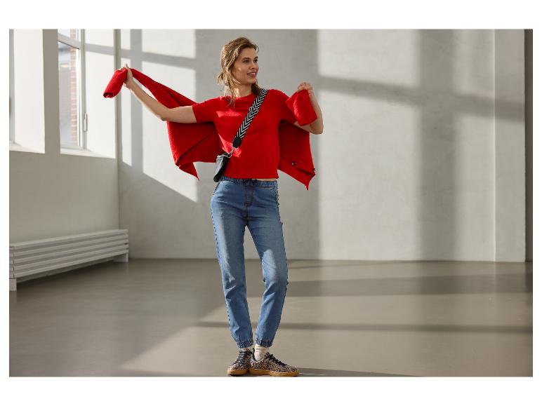Femme en pull rouge, jean bleu et baskets léopard, tenant un cardigan rouge.