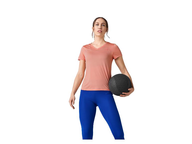 Femme en t-shirt rose et leggings bleus tenant un ballon d'exercice.