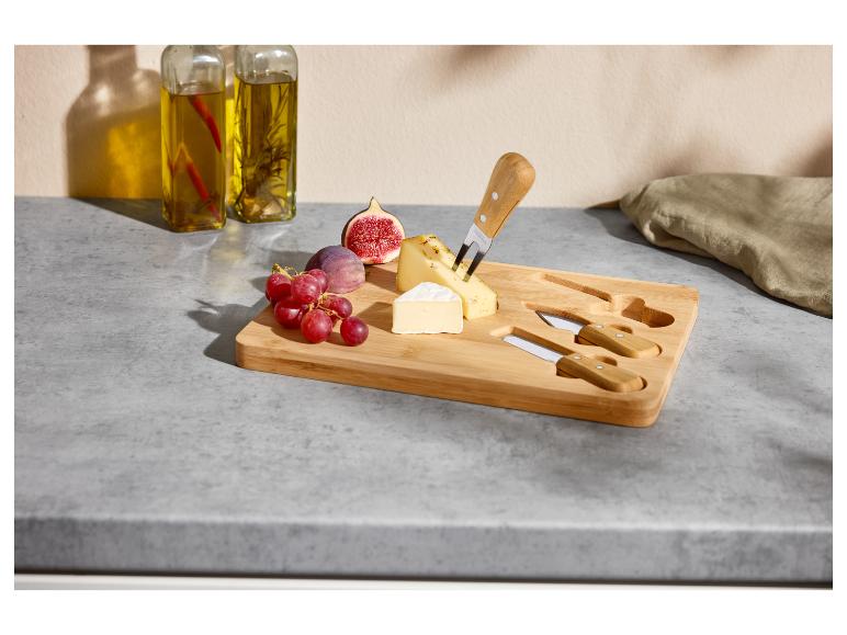Planche à fromage en bois avec fromages, figues, raisins et couteaux sur un comptoir.