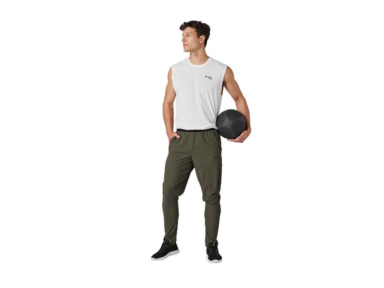 Homme en débardeur blanc et pantalon de survêtement kaki, tenant un ballon lesté noir.
