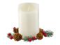 Une bougie blanche avec un effet de flamme, entourée de branches de pin, de pommes de pin et de baies rouges.