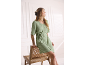 Femme en robe vert clair à manches courtes avec ceinture à nouer, assise sur une chaise en osier.