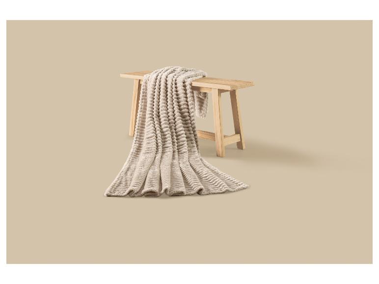 Plaid beige doux à texture bulle drapé sur un banc en bois.