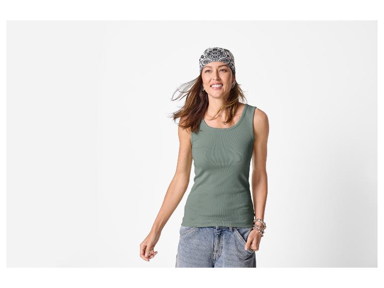 Femme en débardeur côtelé vert, short en jean et bandana à motifs, souriante.