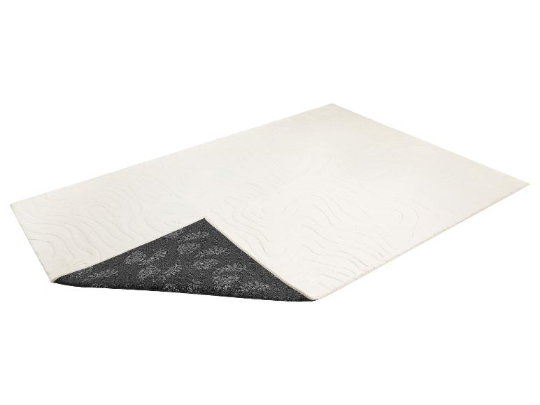 Tapis de bain blanc cassé avec un motif ondulé et un revers antidérapant gris foncé à motif floral.