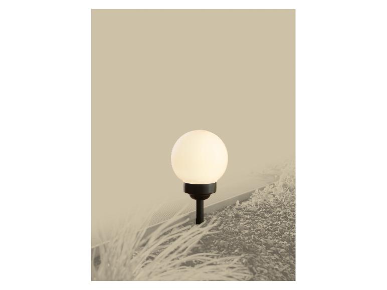 Une lampe de jardin sphérique éclaire un parterre de paillis et d'herbe.