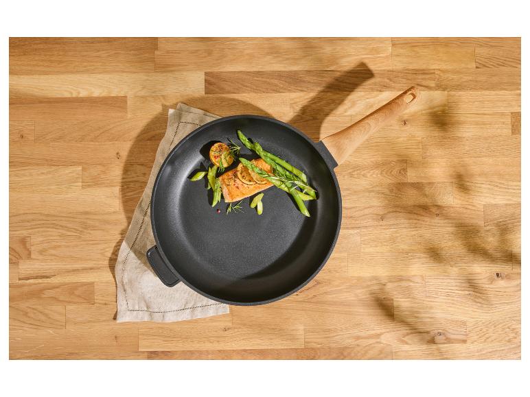 Poêle avec saumon, asperges et citron sur une table en bois.