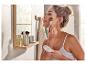 Une femme se maquille avec un pinceau et une poudre compacte dans une salle de bain.