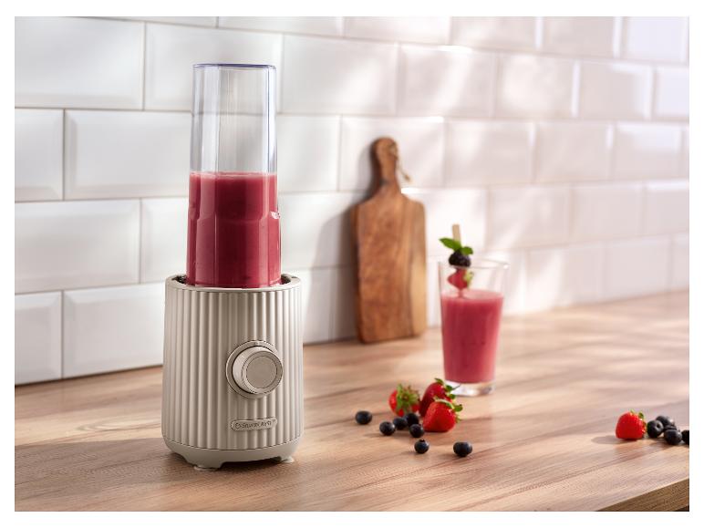 Mixeur SilverCrest avec smoothie rouge, fruits et un verre sur un comptoir en bois.