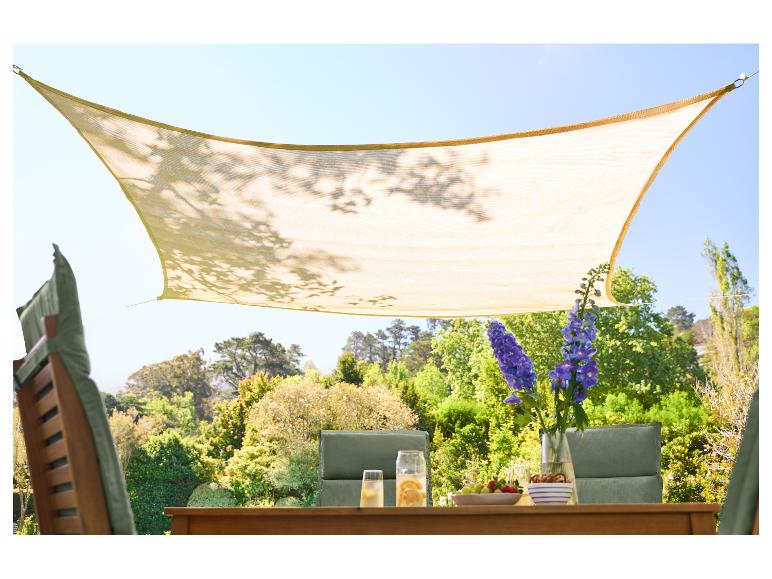 Voile d'ombrage beige au-dessus d'une table de jardin en bois avec boissons et collations.