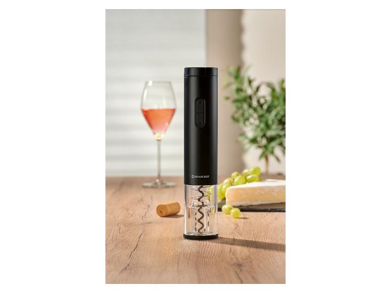 Tire-bouchon électrique noir sur une table en bois avec du vin, du fromage et des raisins en arrière-plan.
