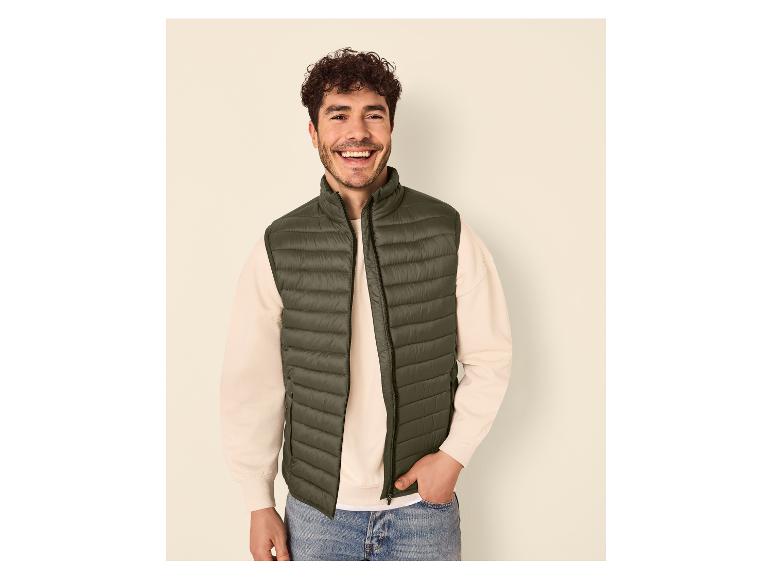 Homme souriant en gilet matelassé vert foncé, sweat-shirt clair et jean.