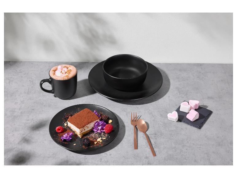 Vaisselle noire avec dessert, chocolat chaud et guimauves sur une table grise.