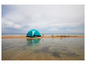 Une tente bleue sur une plage de sable avec un petit château de sable