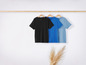 Trois t-shirts, noir, bleu foncé et bleu clair, suspendus à un cintre en bois.