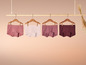 Quatre paires de culottes roses à pois, rayures et unies, suspendues à une barre en bois.