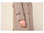 Manteau beige avec boutons et une main portant une bague dorée.