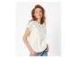 Femme en blouse blanche brodée et jean, posant sur un fond blanc.