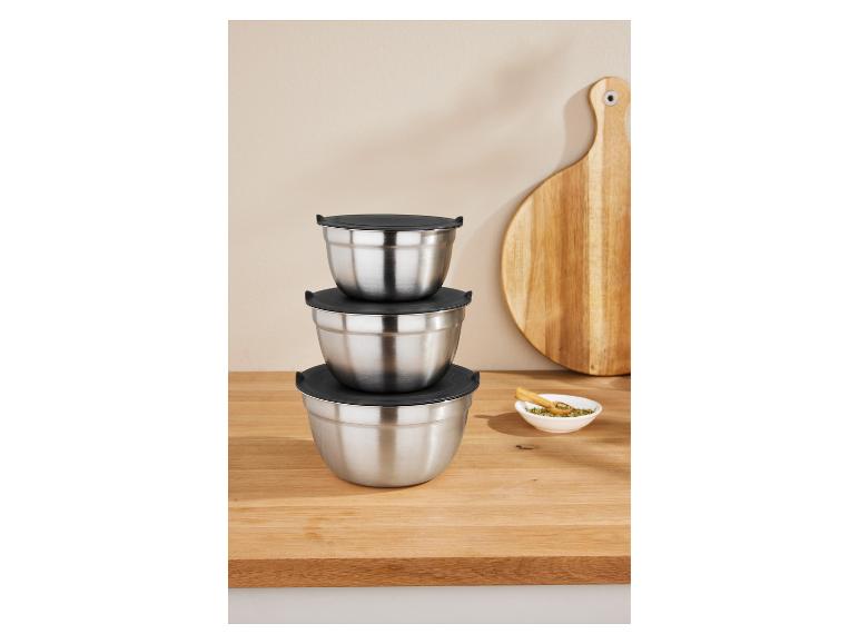 Trois bols mélangeurs empilés en acier inoxydable avec couvercles noirs sur une table en bois.