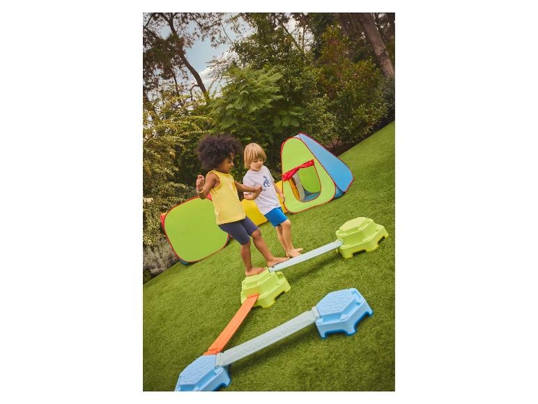 Enfants jouant sur une poutre d'équilibre en extérieur avec des tentes de jeu.