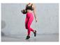 Une femme en leggings roses et un soutien-gorge de sport noir tient un ballon de fitness.