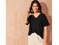 Une femme porte un t-shirt noir et un pantalon blanc.
