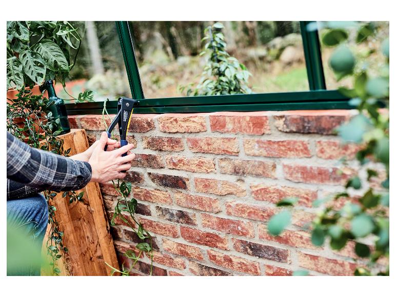 Personne utilisant une pince à riveter LIVARNO® sur un mur de briques dans une serre.