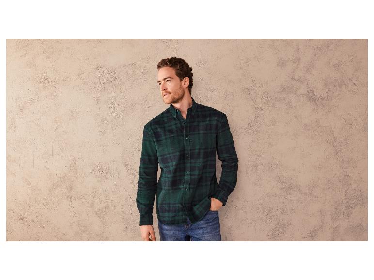 Un homme portant une chemise à carreaux verts et un jean.