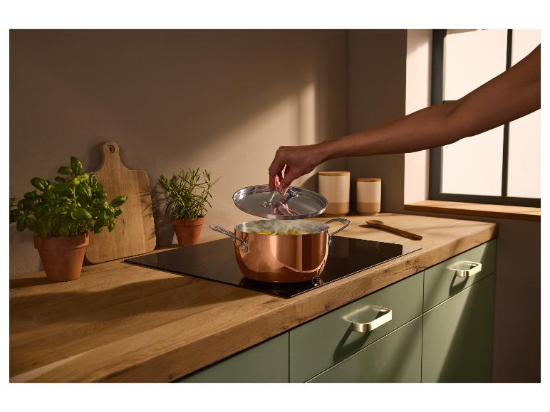 Cuisine avec plan de travail en bois, armoires vertes et casserole en cuivre sur la plaque.