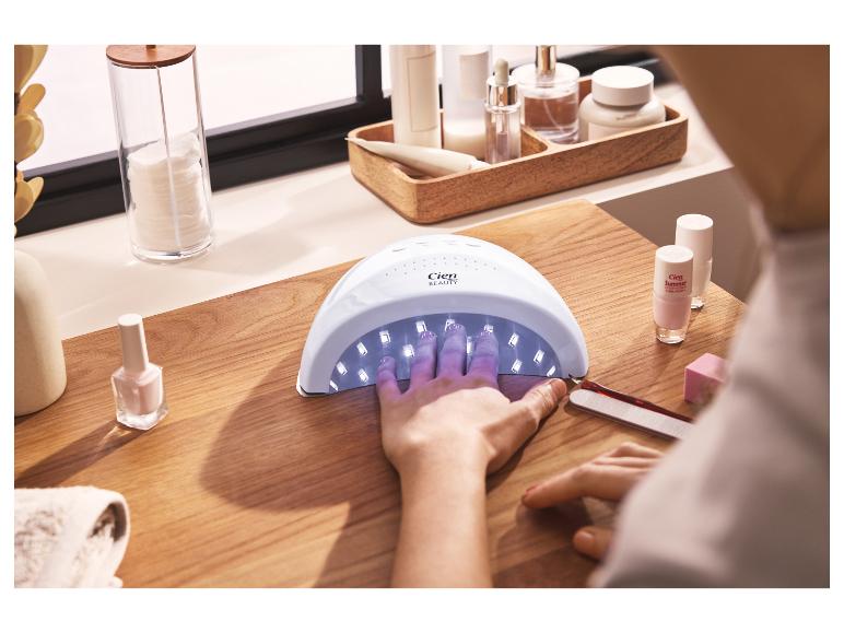 Femme séchant ses ongles sous une lampe UV, avec vernis et accessoires de manucure.